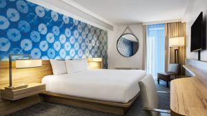 View Of Hotel Room Showing Two Beds, Nightstands With Lamps, Dresser, Small Desk With Chair, And A Small Sitting Area Near The Window Inside Harrah’s Las Vegas