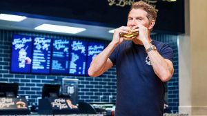 Bobby Flay standing in front of Bobbys Burgers eating a burger