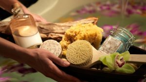 Photo Of A Basket Of Spa Essentials Being Held Over A Bath Filled With Flower Petals