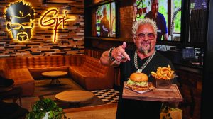 Guy Fieri is holding a burger and fries in the Flavortown restaurant.