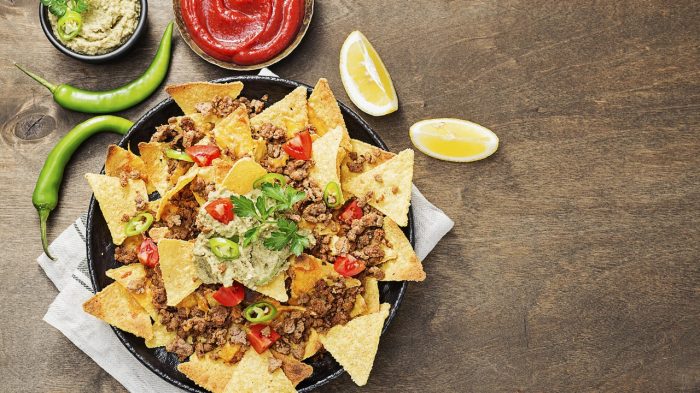 Corn chips nachos with fried minced meat and guacamole on wooden background.