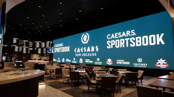 Seating area, odds screens, and large TV screen at Caesars Sportsbook.