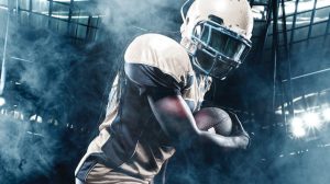 Football player holding a football with stadium lights in the background