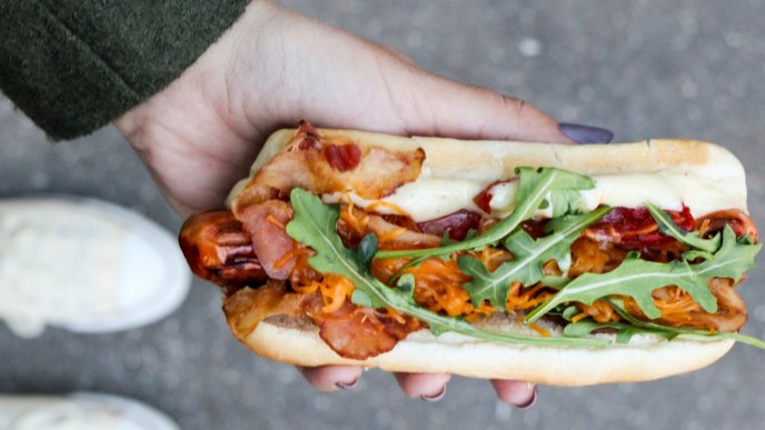 Person holding a hotdog with bbq meat and arugula topping. Person holding a hotdog with bbq meat and arugula topping.