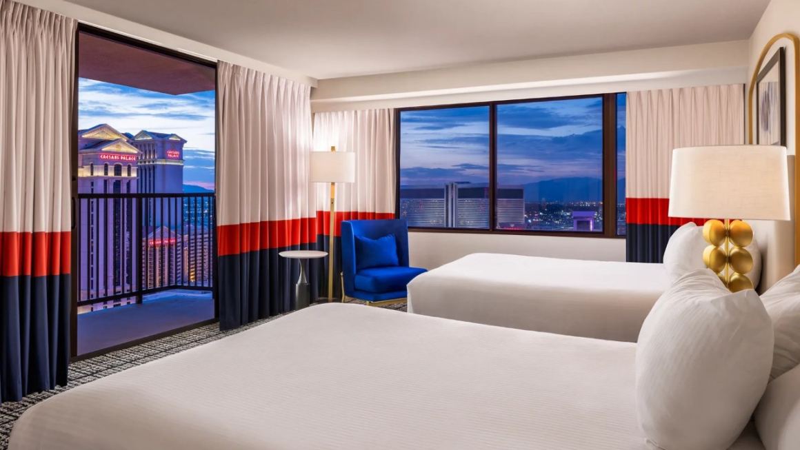 Photo of Paris Las Vegas Versailles Tower Balcony Room with two queen beds, chair with table, nightstand with lamp,  and balcony with North facing strip views