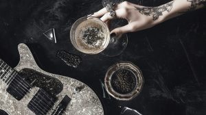 A tattooed hand reaching for a drink with a glitter guitar in the corner