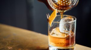 Cocktail shaker pouring cocktail into a rocks glass.