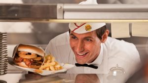 Johnny Rocket Employee Handing A Plated Cheeseburger And Fries Over The Counter Inside Caesars Windsor